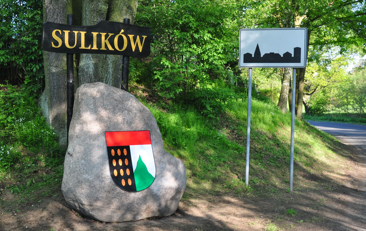 Wjazd do miasta Sulików. Kamień z herbem i tablica informacyjna. Znak terenu zabudowanego.